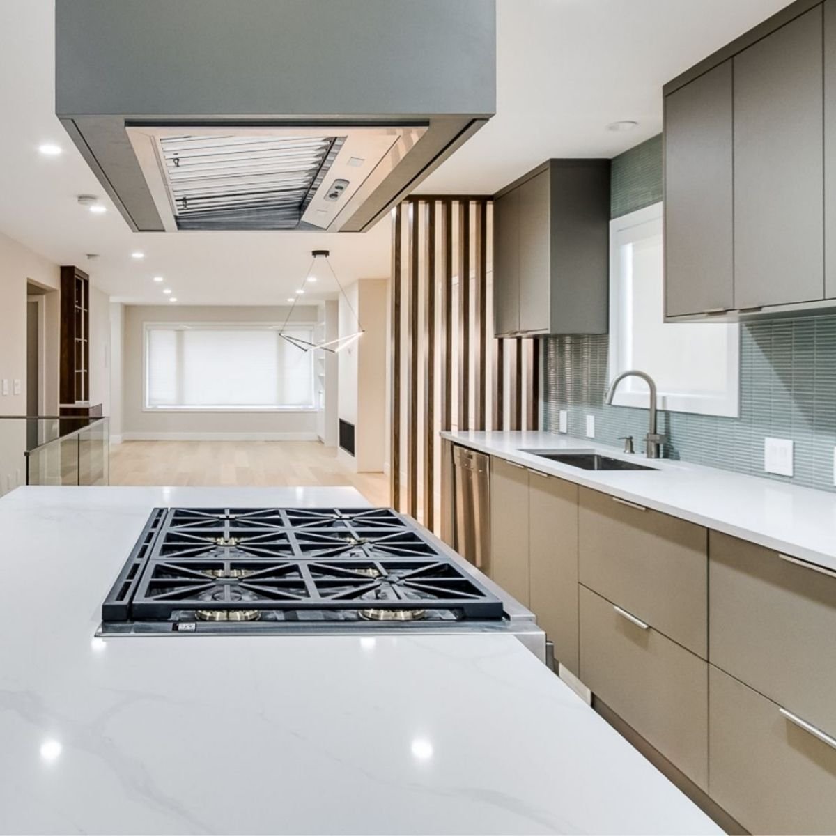 Modern kitchen with taupe cabinetry, white countertops, gas cooktop, and wood slat divider. Greater Vancouver.