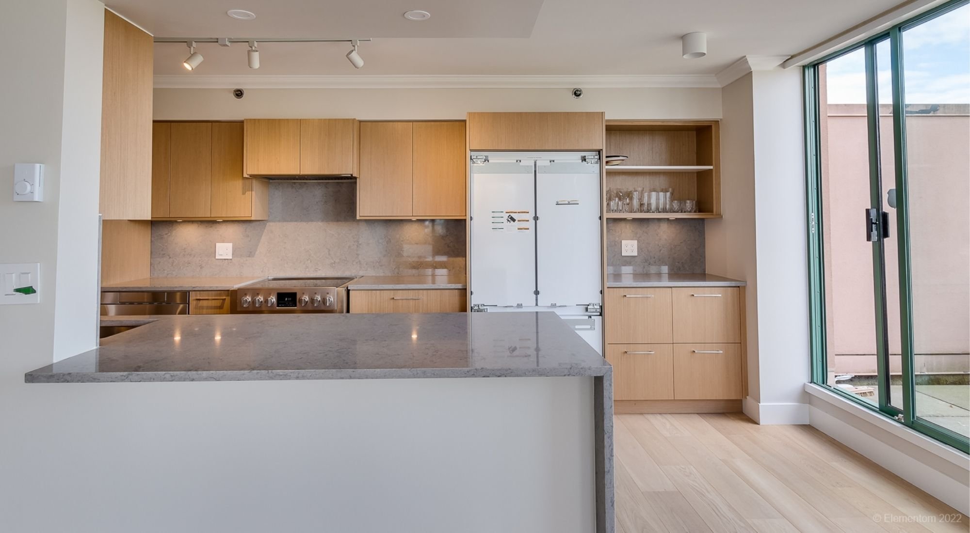 Modern kitchen with light wood cabinetry, stone peninsula, and large windows, Greater Vancouver - Optimized.