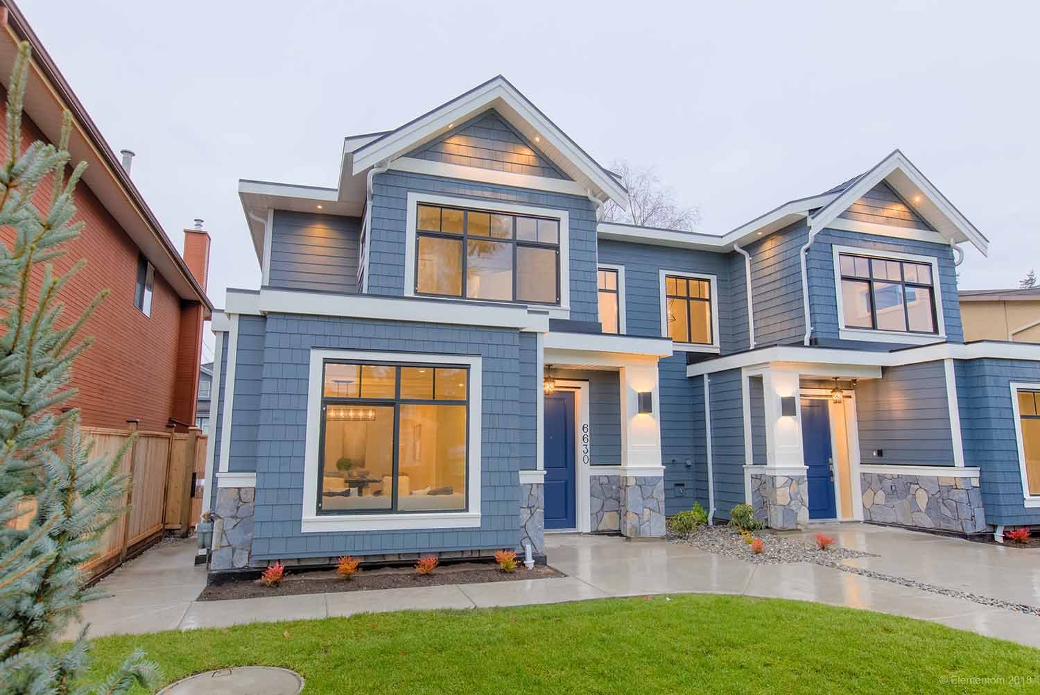 Blue two-storey duplex exterior with matching entrances, white trim, stone accents, large windows, and landscaped front yard.