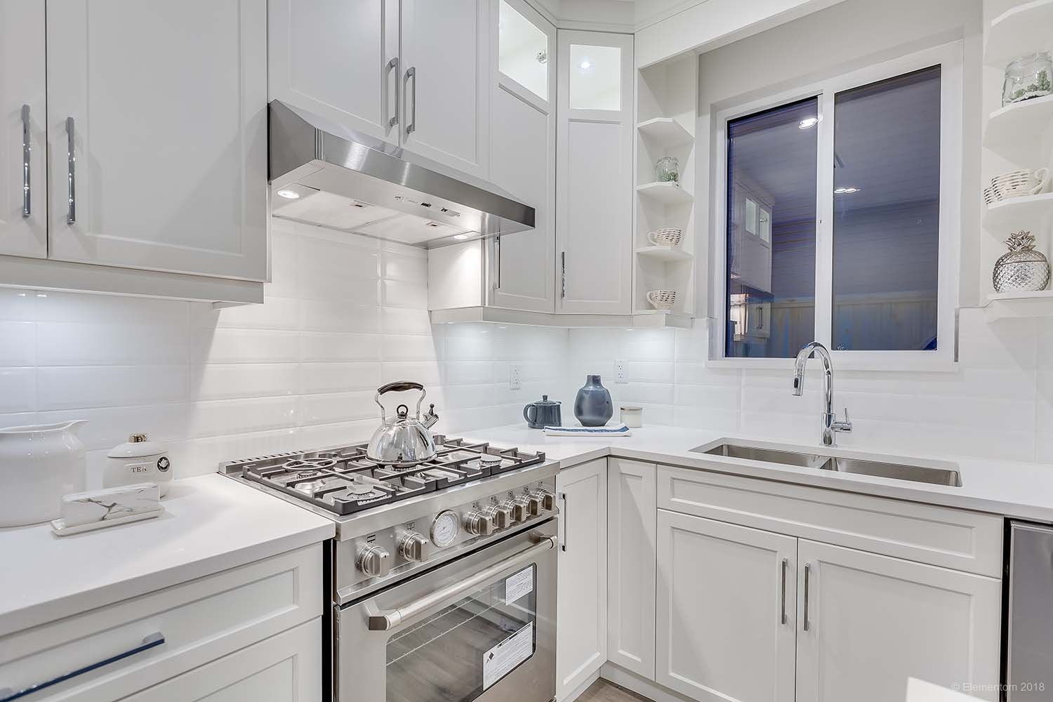Bright white kitchen with gas range, stainless steel hood, quartz countertops, farmhouse-style sink, and ample cabinetry.