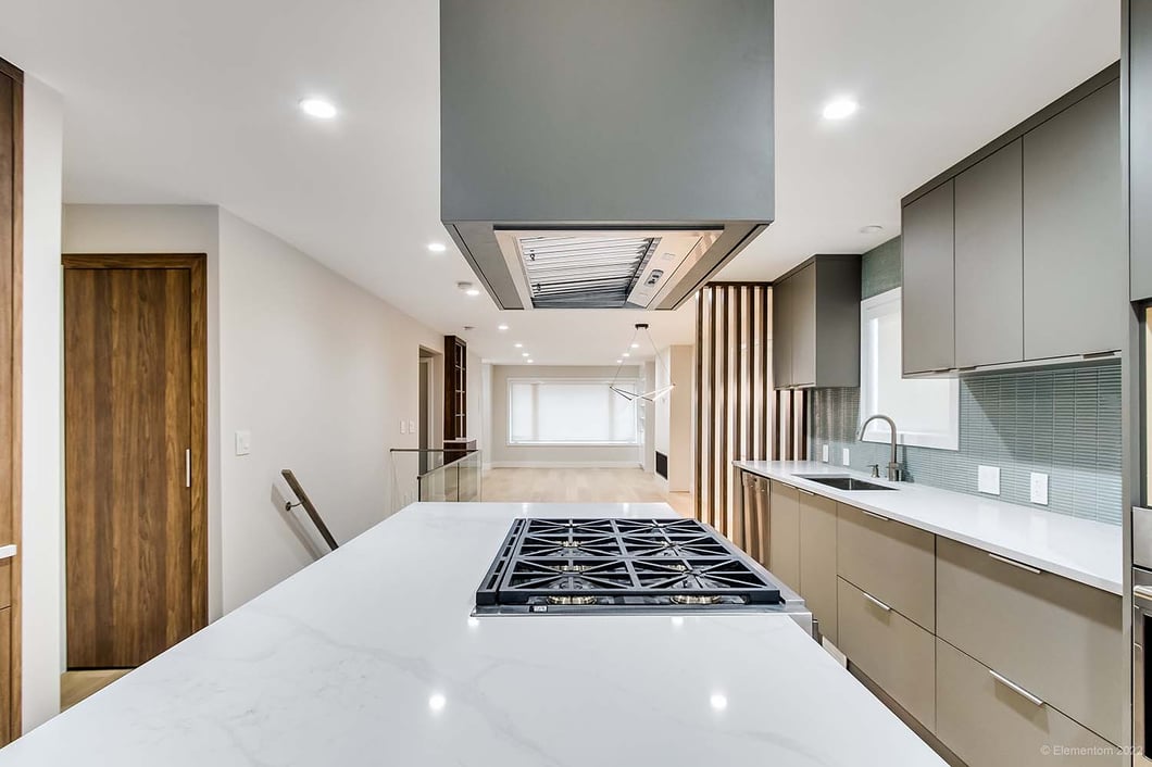 Modern kitchen with a large quartz island, built-in gas cooktop, ceiling-mounted range hood, wood cabinetry, and sleek finishes.