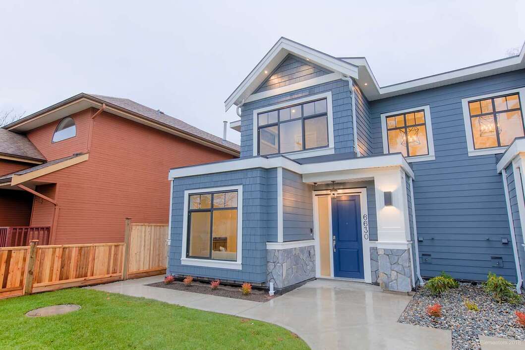 Two-storey blue home exterior with white trim, stone accents, covered entry, front lawn, and landscaped walkway.