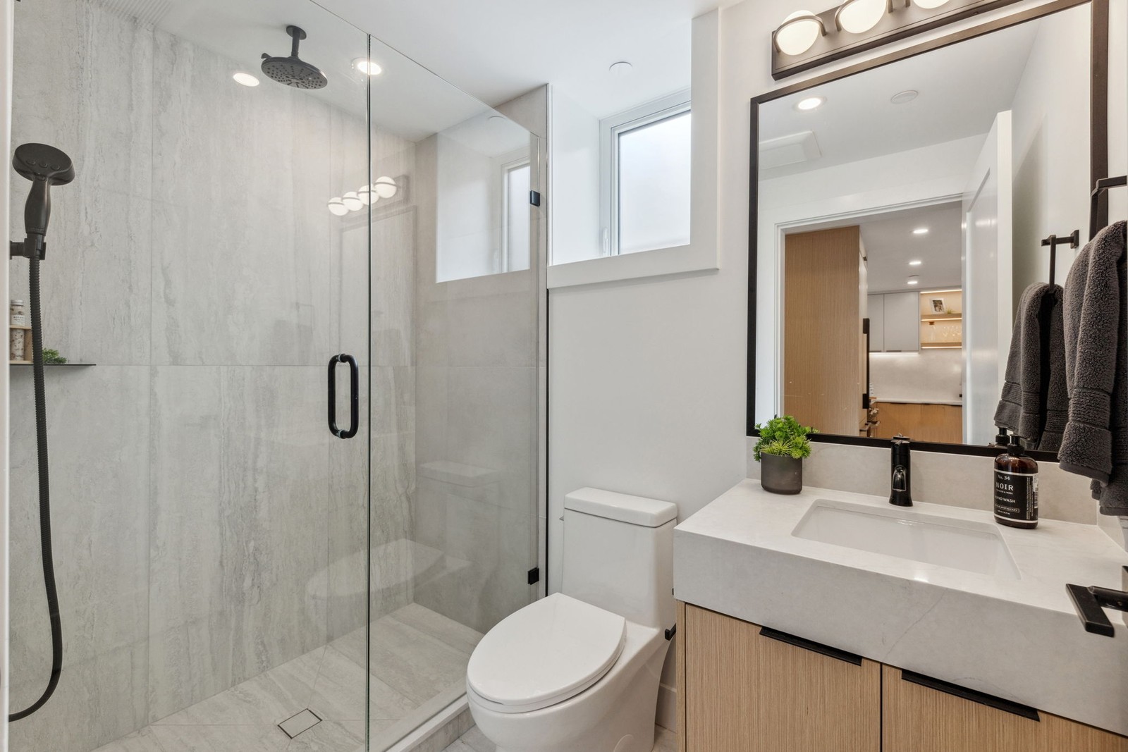 Modern bathroom with glass walk-in shower, light wood vanity and black fixtures in a Vancouver home