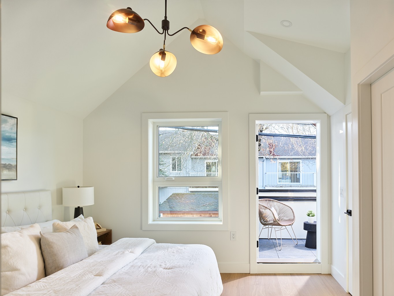 Vancouver primary bedroom with vaulted ceiling, black chandelier, and door to a private balcony
