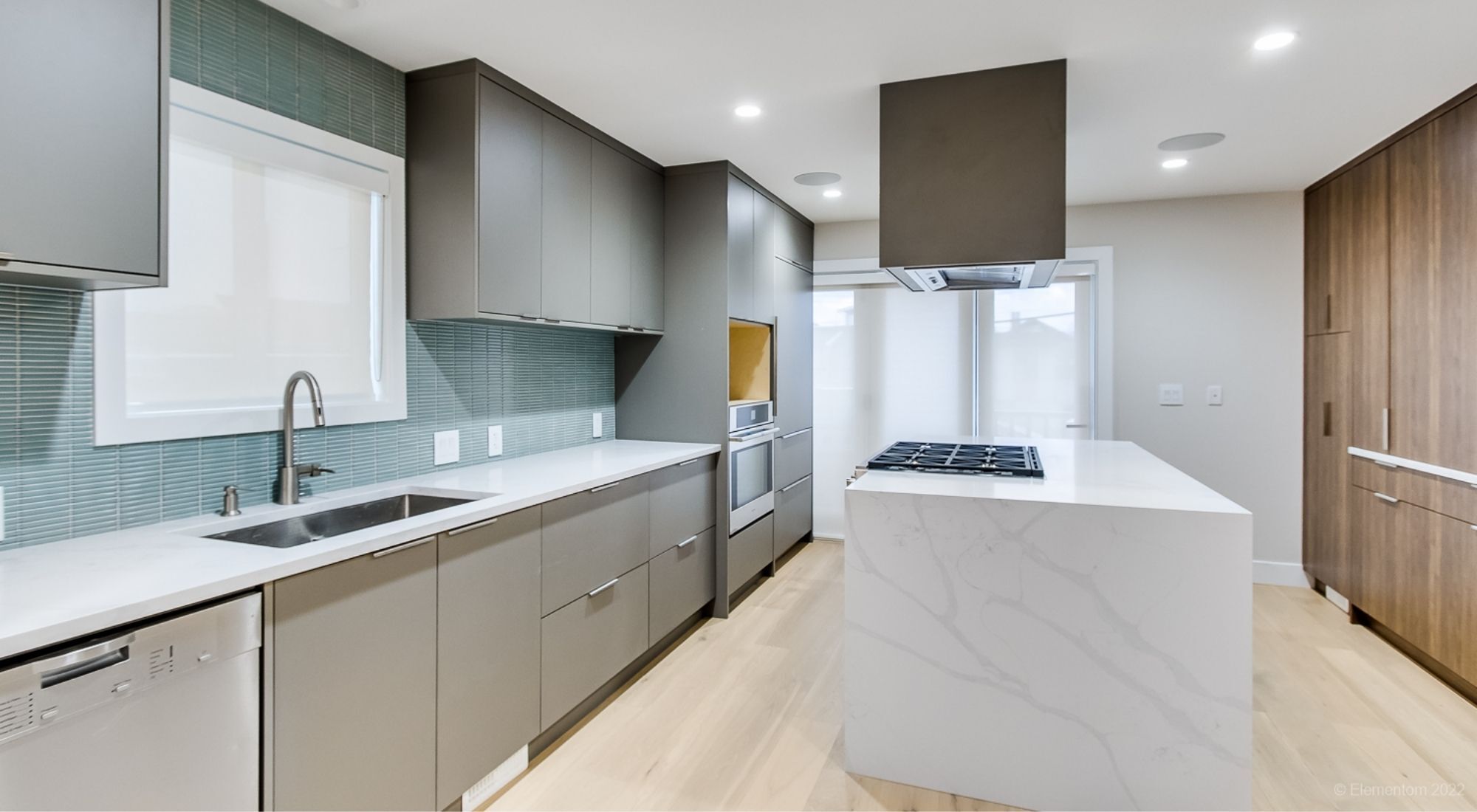 Modern kitchen with white island, gray cabinetry, green backsplash, and wood pantry storage + Greater Vancouver - op