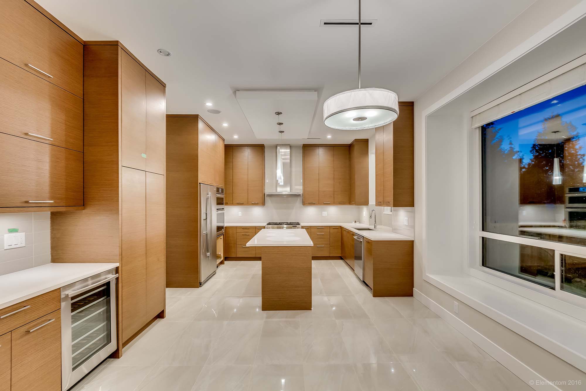 Bright custom home kitchen with warm wood cabinetry, large island, modern lighting, and expansive windows in Greater Vancouver